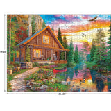 A scenic image of a log cabin by a lake with a canoe, surrounded by trees and colorful flowers. A sunset sky with clouds and a flying bird are in the background. Dimensions: 26.625" x 19.25". Product Name: RoseArt - My Happy Place - Forest Cabin Home - 1000 Piece Jigsaw Puzzle