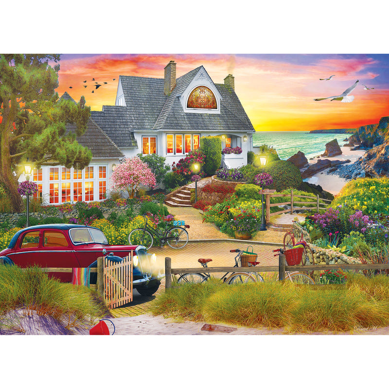 A coastal house with a colorful garden is shown at sunset. Bicycles, a red car, and a path leading to the beach are present, with birds flying in a vibrant sky. This is captured beautifully in the RoseArt - My Happy Place - Seaside Hill - 1000 piece jigsaw puzzle.