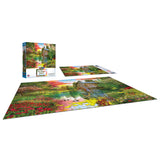 A completed RoseArt - My Happy Place - Sunset at the Mill - 1000 Piece Jigsaw Puzzle depicting a colorful garden scene with a watermill is laid out next to its box and an unassembled portion of the puzzle.