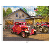 A completed RoseArt - American Nostalgia - Hot Rod Flames - 550 Piece Jigsaw Puzzle showing a classic car and motorcycle in front of a vintage mechanic shop with the American flag displayed. The puzzle measures 18x24 inches.