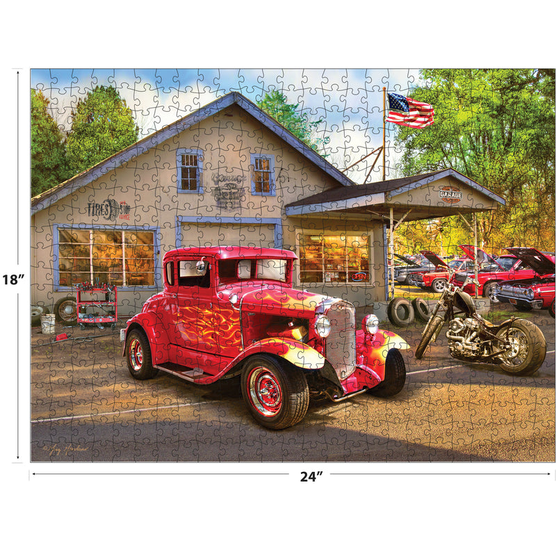 A completed RoseArt - American Nostalgia - Hot Rod Flames - 550 Piece Jigsaw Puzzle showing a classic car and motorcycle in front of a vintage mechanic shop with the American flag displayed. The puzzle measures 18x24 inches.
