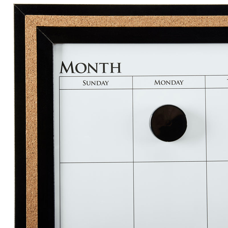 Close-up of a framed monthly Board Dudes Dry Erase Calendar Cork Magnetic Combo 22 x 18 inches: Stylish Organization for Any Space. The calendar shows columns for Sunday, Monday, and Tuesday. A black circular magnet is placed in the Monday column.