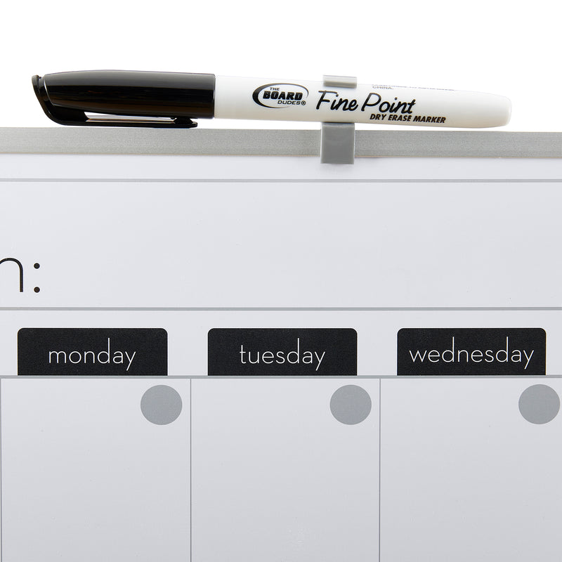 A Fine Point dry erase marker is placed horizontally on a clip at the top of a Board Dudes Dry Erase Magnetic Calendar 16x20 INCH: Elevate Your Organizational Game showing spaces for Monday, Tuesday, and Wednesday.
