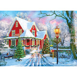 Colorful illustration of a red house decorated for Christmas, surrounded by snow-covered trees and a snow-covered yard, with a lit lamppost, a decorated Christmas tree, and snowman in the center – RoseArt - Kodak Premium - Christmas at Home - 1000 Piece Jigsaw Puzzle.