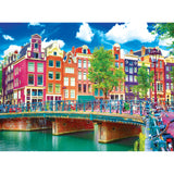 A vibrant canal scene in Amsterdam with colorful buildings, a bridge, and numerous bicycles lined along the railing on a sunny day is depicted in the RoseArt - Kodak Premium - Colorful Waterfront Buildings, Amsterdam - 1000 Piece Jigsaw Puzzle.