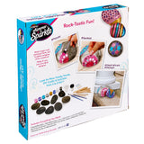 The image shows a Cra-Z-Art Shimmer 'n Sparkle Metallic Mania Rock Art labeled "Rock-Tastic Fun!" The kit includes paint, brushes, rocks, and instructions to create decorative painted rocks. Examples of completed projects are shown on the box.