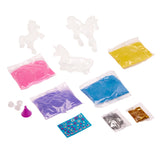 The image shows a Shimmer 'n Sparkle Sparkling Unicorn Sand Art Creations kit with clear unicorn molds, bags of colored sand (purple, pink, blue, yellow), small pouches of glitter, a funnel, small bottle caps, and a sticker sheet.