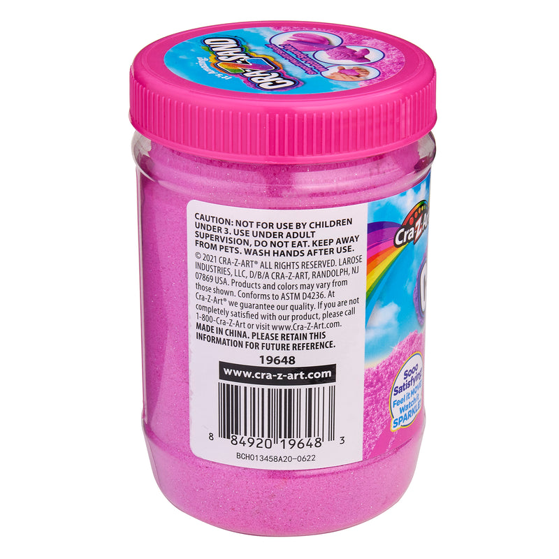 A jar of Cra-Z-Sand Pink Glitter Sand, 1.5 LB Tub in pink, with a purple screw-on lid. The label includes usage cautions, ingredients, and manufacturer information.