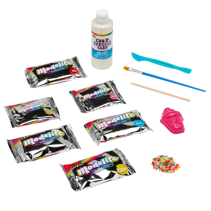 A collection of crafting supplies including five packets of Cra-Z Crackle Clay, a bottle of glaze, a paintbrush, a sculpting tool, a plastic tool, a small bag of colorful beads, and a pink mold in the shape of a shoe.