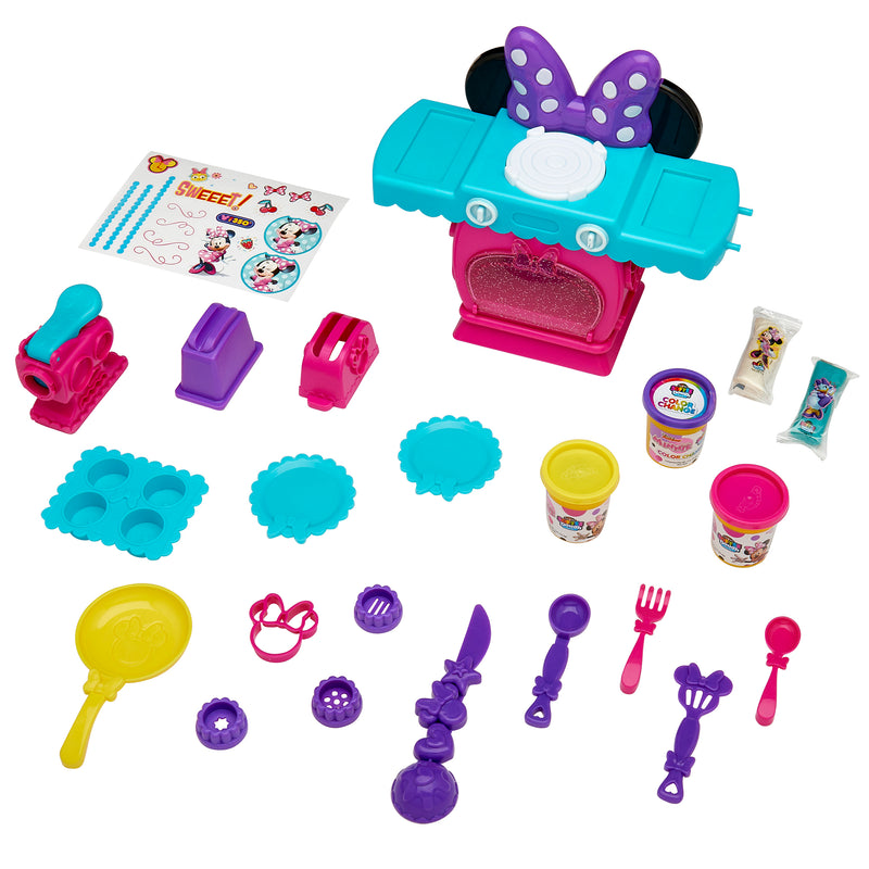 A colorful children's baking play set featuring a toy oven, baking molds, utensils, containers of play dough, and a decorative sticker sheet called the Disney Minnie Softee Dough Color Change Kitchen.