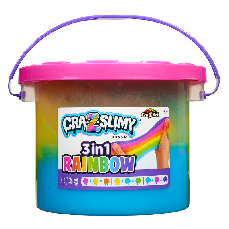 A bucket of Cra-Z-Slimy Bucket TRICOLOR RAINBOW 48 OZ, weighing 3 lb (1.36 kg), with a pink lid and purple handle. The label features a hand holding rainbow-colored slime.