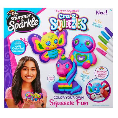 Product packaging for "Shimmer 'n Sparkle Cra-Z-Squeezies Color Your Own Squeezie Fun" showing colorful, squeezable toys and markers. The box features a girl holding the toys and highlights they are scented, soft to squeeze, and for ages 6 and up.