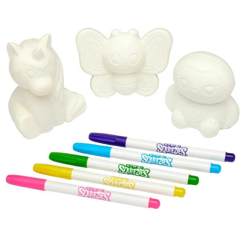 Three white, unpainted figurines shaped like a unicorn, butterfly, and animal, with five colored markers (pink, green, blue, yellow, and purple) placed in front of them—Shimmer 'n Sparkle Cra-Z-Squeezies Color Your Own Squeezie Fun.