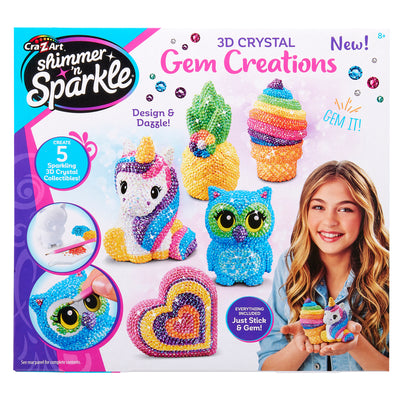 A box of Shimmer 'n Sparkle 3 D Crystal Gem Creations, showing various colorful gem-covered models, including a unicorn, owl, ice cream, and rainbow heart. A girl smiles holding the rainbow heart.