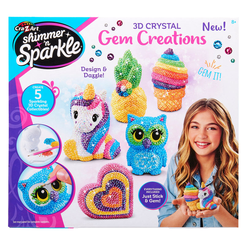 A box of Shimmer 'n Sparkle 3 D Crystal Gem Creations, showing various colorful gem-covered models, including a unicorn, owl, ice cream, and rainbow heart. A girl smiles holding the rainbow heart.