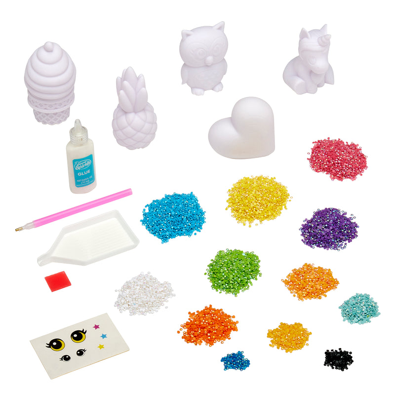 A Shimmer 'n Sparkle 3 D Crystal Gem Creations kit featuring bead art supplies, including white figurines, a bottle of glue, multi-colored beads, a glue pen, a tray, adhesive squares, and a pack of decorative eyes.