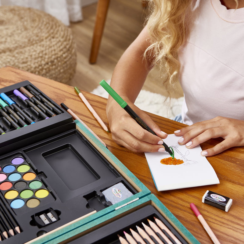 Girl drawing with the RoseArt Timeless Creations Premium Sketch & Design 70+ piece art set with colored pencils, markers, pastels, drawing and charcoal pencils, sketch pad and teal wooden carrying case.