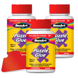 Three bottles of RoseArt - 4.5 oz Puzzle Glue 3 pack with red screw-on caps and labels that read, "Puzzle Glue" and "Saves, Laminates & Preserves Finished Jigsaw Puzzles." One red glue spreader is also shown.