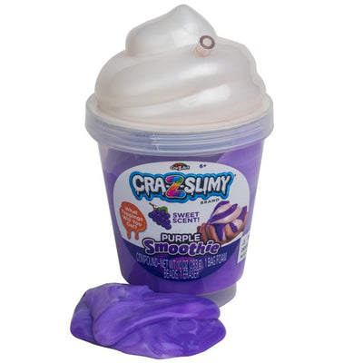 Plastic container of Cra-Z-Slimy Purple Smoothie with a slime spill next to it. The container has a whipped cream-like lid and a sweet scent label.