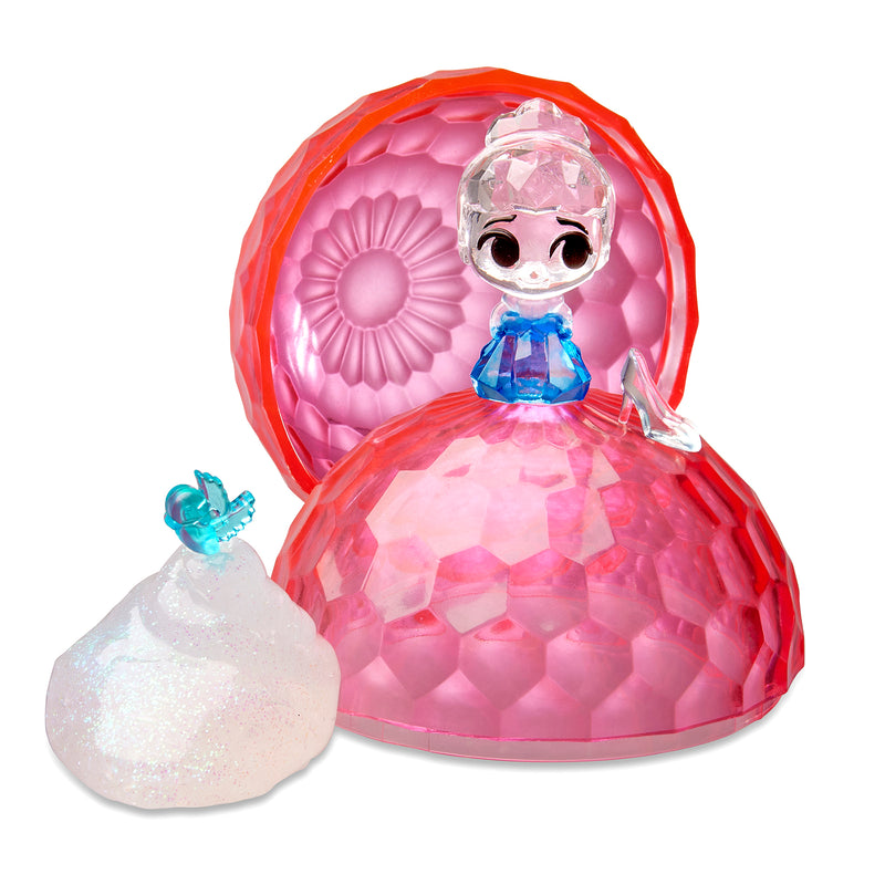 Uncover the enchanting Disney Crystal Surprise Color Change Ball: a toy figure housed within a pink, gemstone-shaped container, reminiscent of a Disney princess with a blue top and translucent hair. The set also features a white accessory adorned with a small blue figurine, enhancing its magical allure.